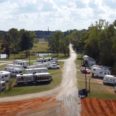 A wide shot of RVs parked at the spacious and well-maintained Bedrock RV Park in Longview, Texas surrounded by trees and open skies.